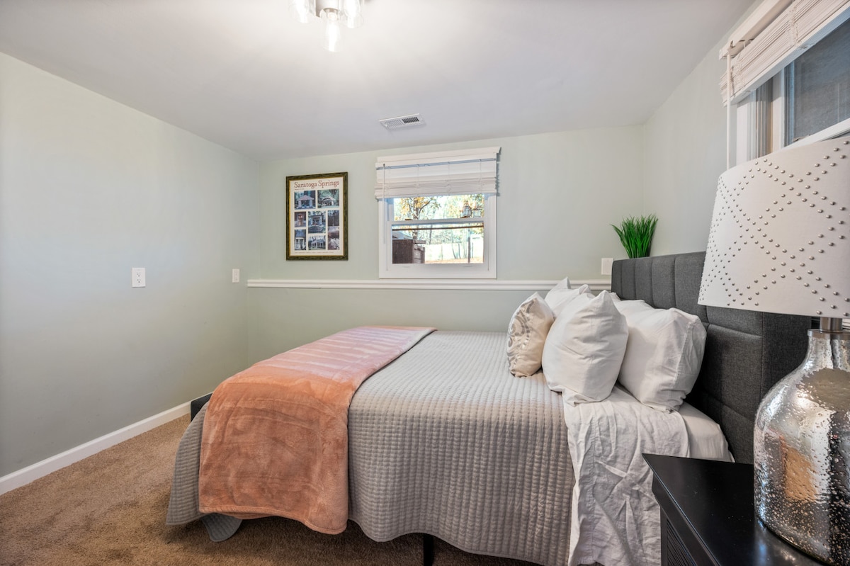 Las paredes de color verde claro, la alfombra lujosa y la cama tapizada en gris crean un ambiente tranquilo. El arte de collage de melocotón y la lámpara plateada aportan personalidad. Perfecto para noches tranquilas o luz suave de la mañana.