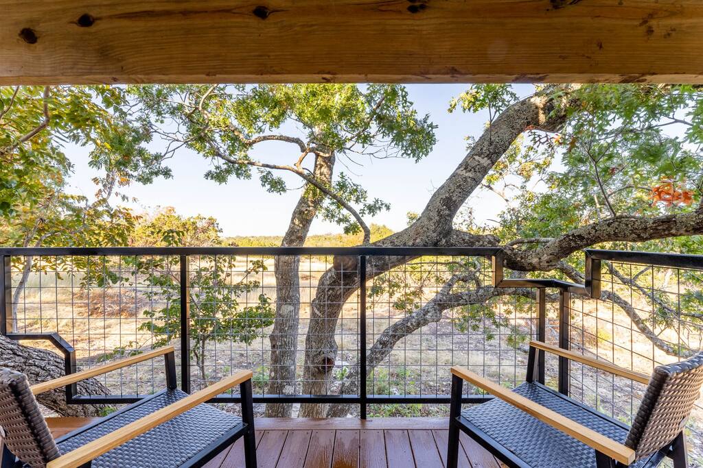 A private observation deck features two wooden chairs facing a scenic view of natural surroundings. Lush trees and open land are visible beyond the railing, allowing guests to connect with nature while enjoying the peace of the outdoors.