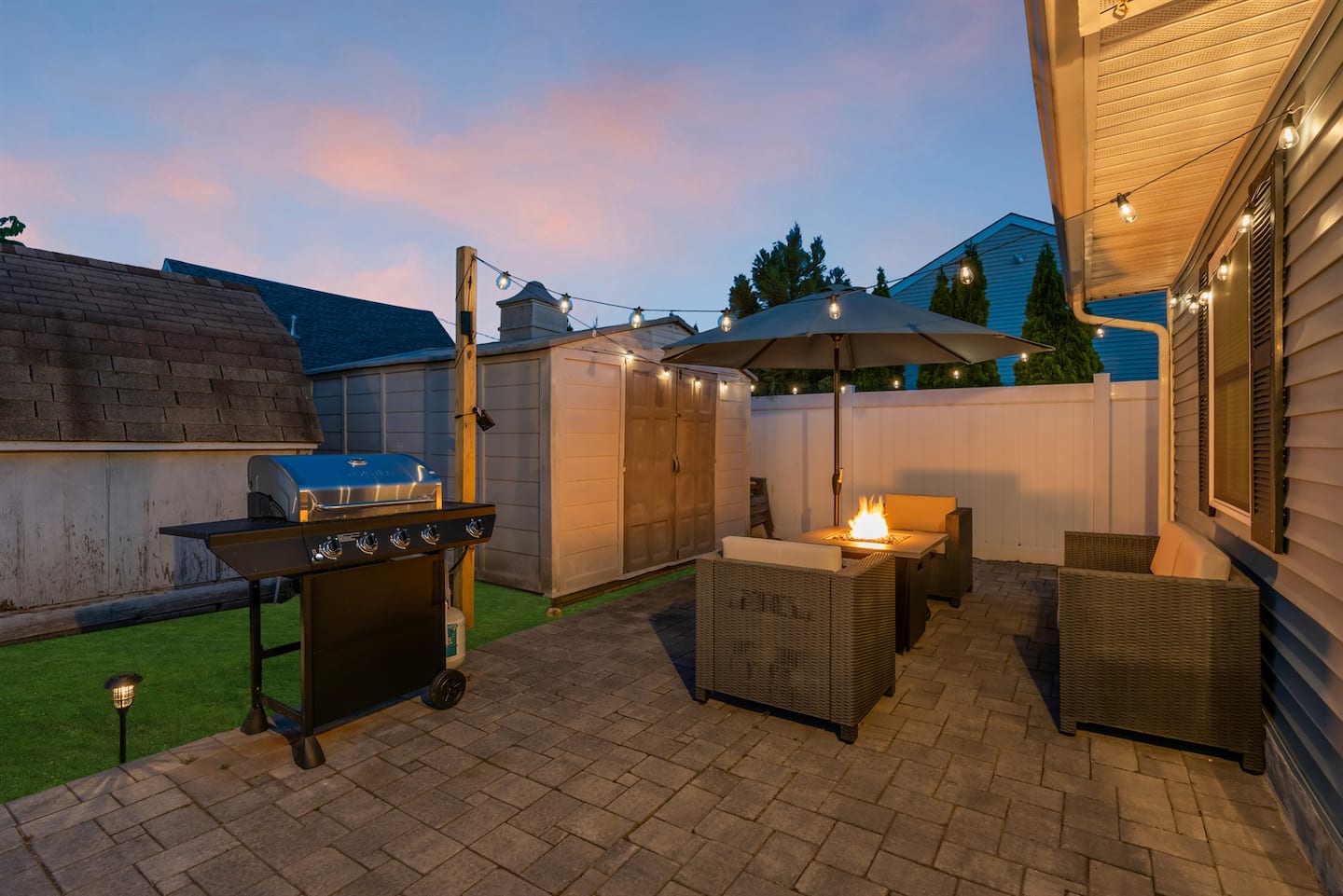 Set up by the fire and let the sky do the work. Wicker sectional, lit firepit, grill ready for the burgers, sunset doing exactly what you came here for.