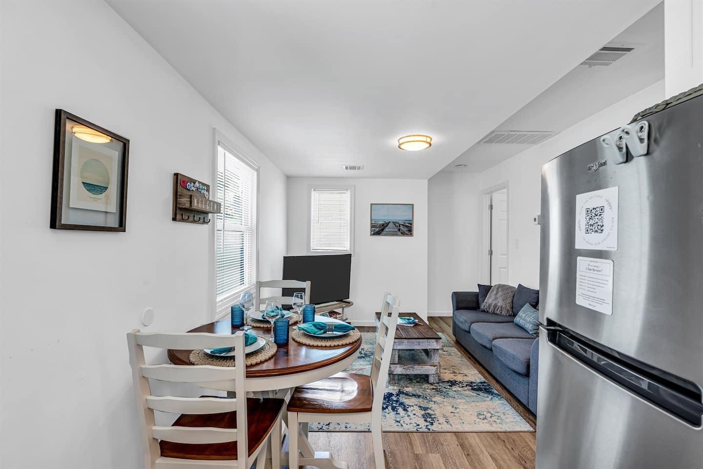 Step inside to a wide-open kitchen + living layout. Sectional in front, gas range and quartz countertops in back, beach art on the walls, green tile breaking up the white.