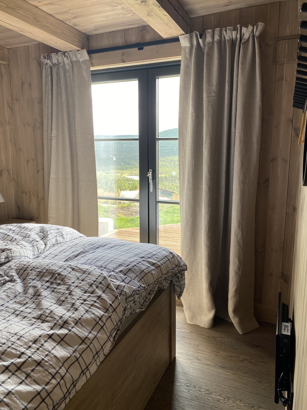 Láka spálňa s teplými drevenými interiérmi, mäkkým osvetlením a pohodlnou posteľou umiestnenou pod veľkým oknom terasy, ktoré ponúka krásne prirodzené svetlo a výhľad.