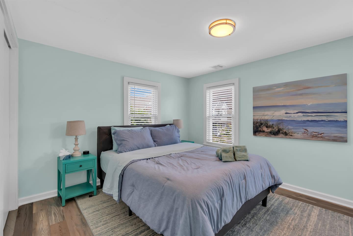Queen bedroom with sage-green walls, teal nightstands and coastal wall art