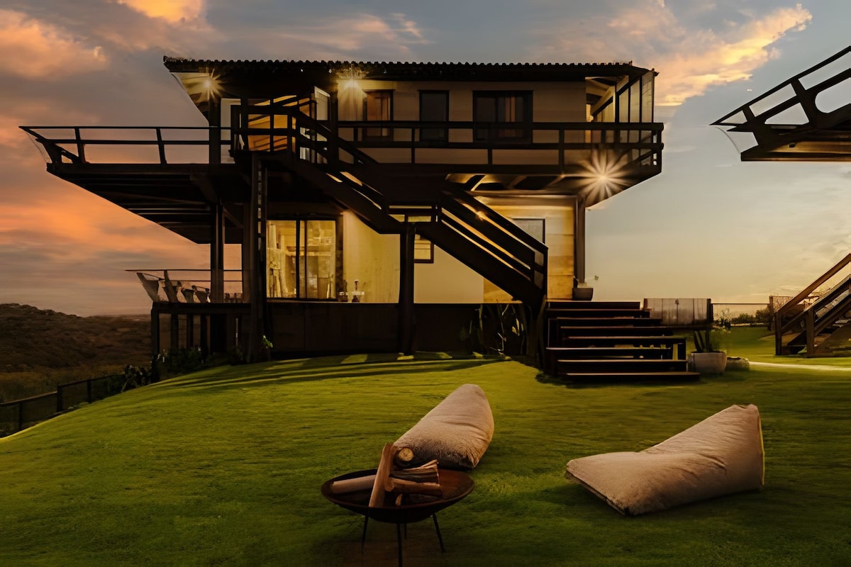 A multi-level structure is presented, featuring large windows that capture natural light. An expansive lawn surrounds the building, with lounge seating positioned on the grass. Warm outdoor lighting casts a gentle glow at twilight, enhancing the serene setting.