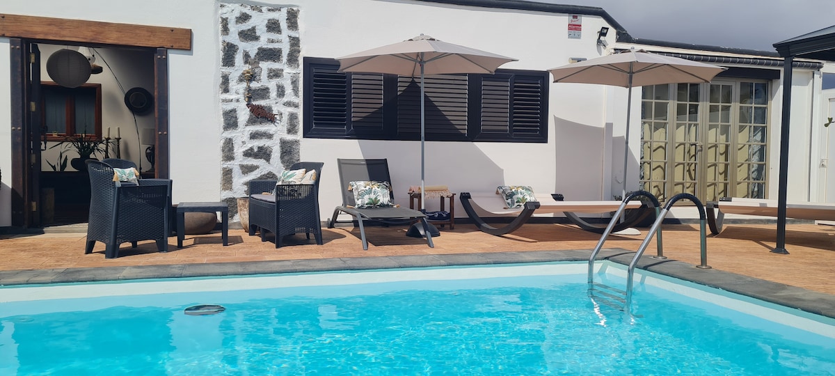 A private pool area features a refreshing blue pool surrounded by comfortable loungers and umbrellas for shade. The space is complemented by a textured wall, and an inviting seating area is arranged nearby, suitable for outdoor relaxation and enjoyment.