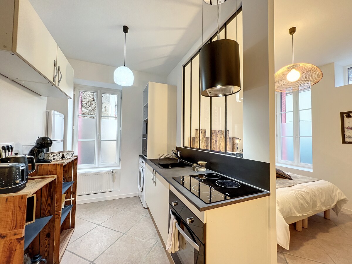 The kitchen area features modern appliances and ample counter space. A washer is integrated into the cabinetry, and a view of the outside is provided through a large window. Soft lighting is accentuated by stylish pendant fixtures, contributing to a functional and inviting atmosphere.