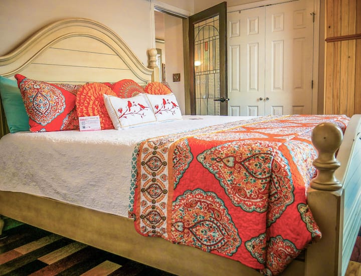 Colorful primary bedroom with king  bed, vintage stained glass door, and bohemian textiles in historic Pensacola bungalow