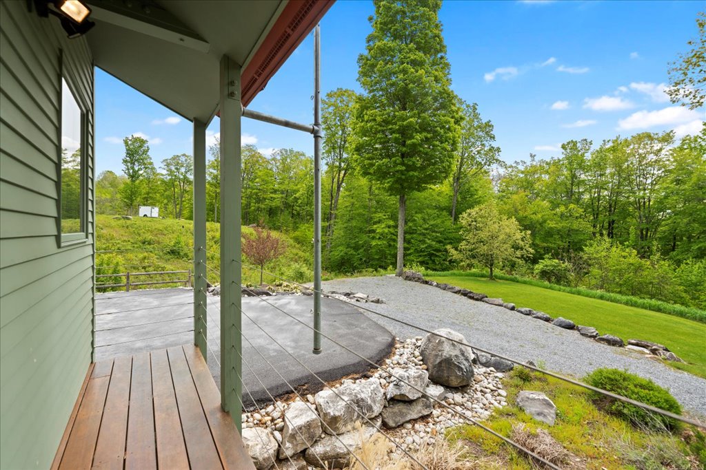 A gravel path leads toward a spacious outdoor area situated amid lush greenery. The scene is framed by trees, with a large area featuring a smooth, dark surface and stone edges. Natural landscaping enhances the tranquil surroundings.