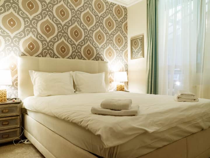 Elegante dormitorio con cama doble, sábanas blancas frescas, papel tapiz de diseño e iluminación cálida: un refugio tranquilo y acogedor para descansar y relajarse profundamente, acceso a Internet de alta velocidad, calefacción para días fríos, ubicación en Colina Marei Residence, Sinaia