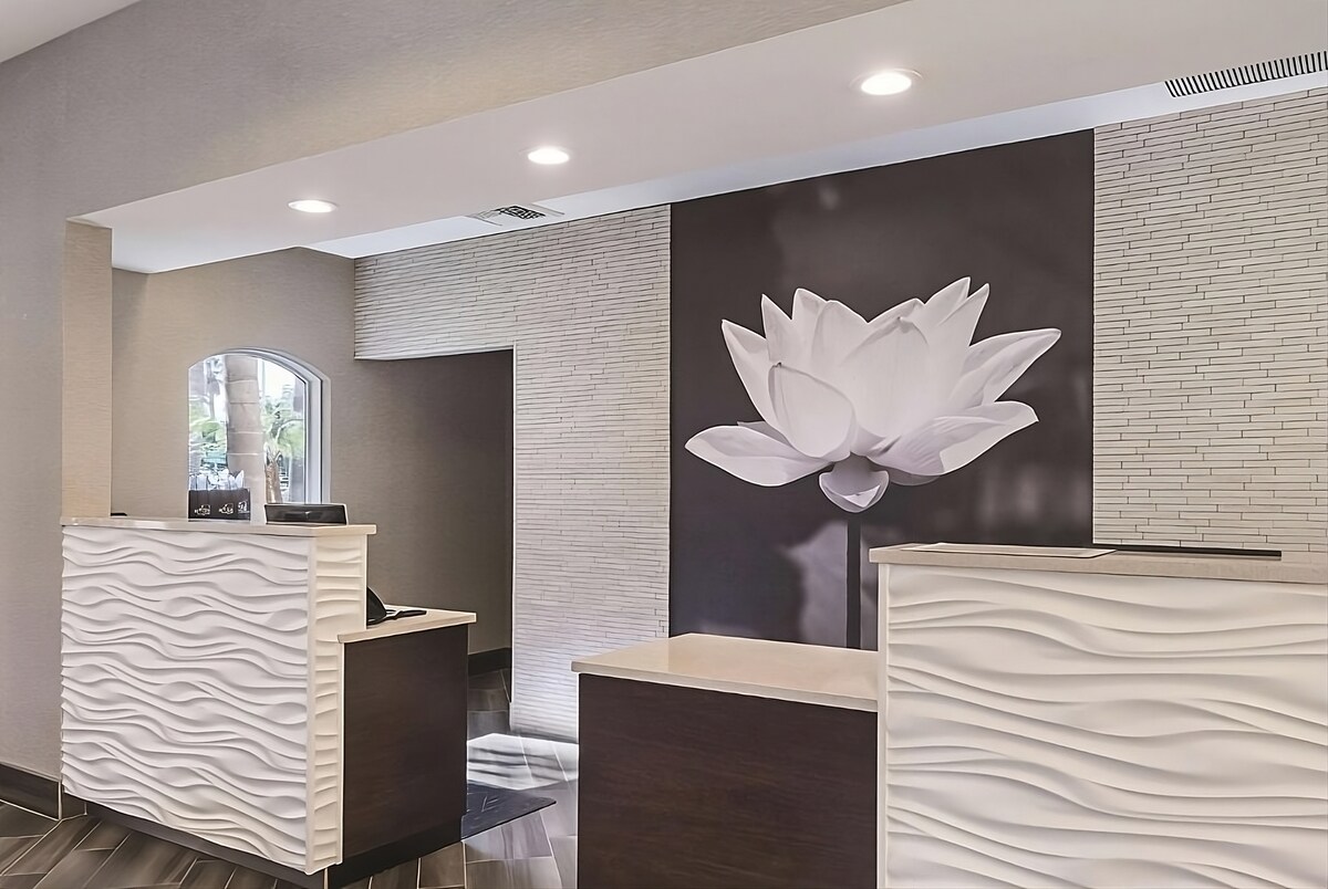 The reception area features a modern design with elegant wave-patterned counters. A large, white lotus flower artwork is displayed on the wall, providing a calming focal point. Soft lighting enhances the welcoming ambiance of the space.