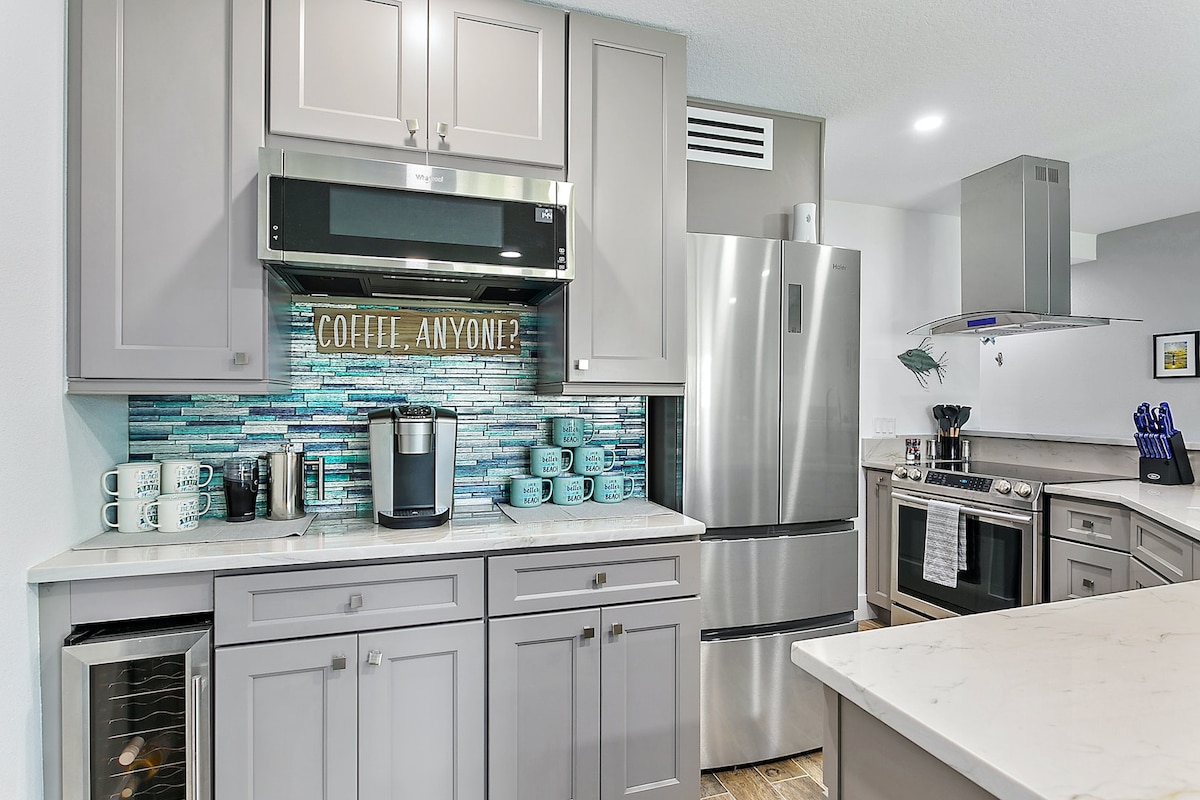 The kitchen features modern cabinetry with a sleek countertop, showcasing stainless steel appliances including a refrigerator and oven. A coffee station, surrounded by blue-tiled backsplash, provides a cozy area for morning routines. Ample storage is available within the drawers and cabinetry.