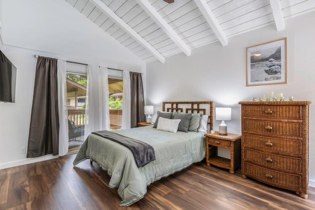 A well-appointed bedroom features a queen-sized bed with soft bedding and decorative pillows. Two bedside tables with lamps flank the bed. A dresser adds functionality, while large sliding glass doors provide access to a private outdoor area. Vaulted ceilings enhance the spacious feel.