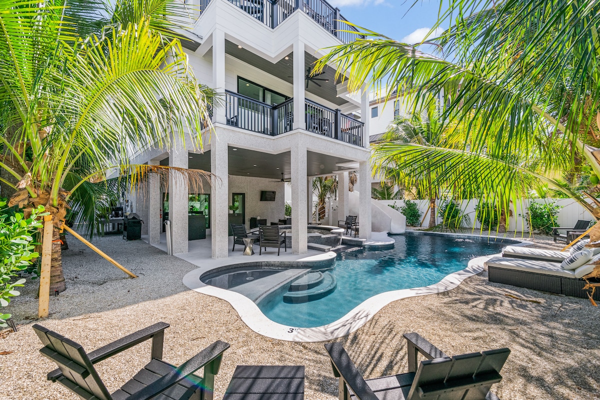A lagoon-style pool is complemented by a jetted spa and surrounded by lounge chairs. Towering palm trees provide a tropical ambiance, while the three-story home with balconies overlooks the spacious backyard, creating a relaxing outdoor retreat.