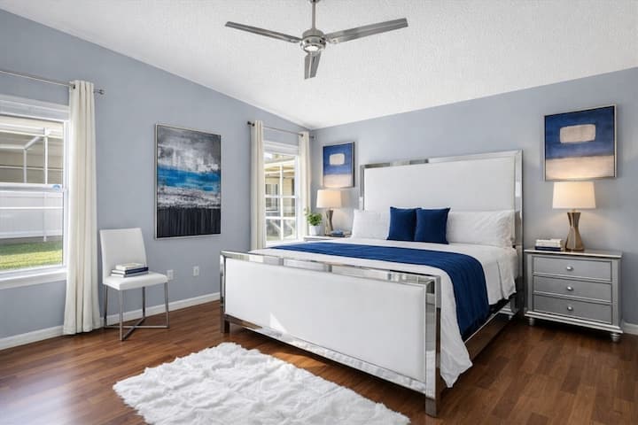 Chambre principale spacieuse avec très grand lit, décor moderne et lumière naturelle provenant de deux fenêtres.