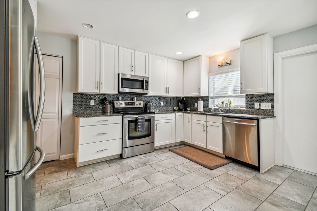 The kitchen features modern cabinetry and stainless steel appliances, including a refrigerator, oven, and dishwasher. A large window allows natural light to illuminate the work surfaces, while a textured backsplash adds visual interest. Ample space is available for meal preparation.