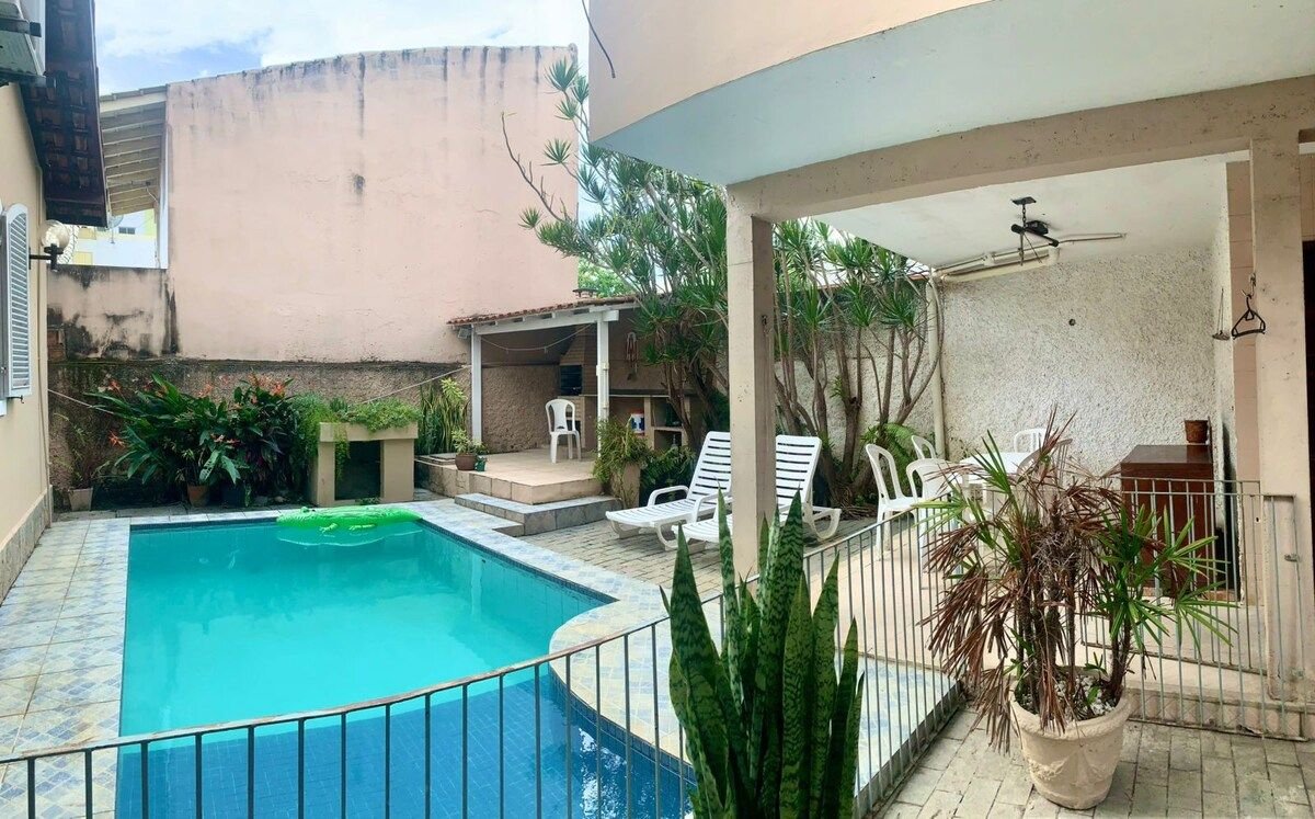 A private outdoor area features a refreshing swimming pool surrounded by tiled decking. Lounge chairs are positioned nearby, with potted plants adding greenery. A shaded seating area is visible, providing space for relaxation and gatherings. The setting conveys a tranquil environment.