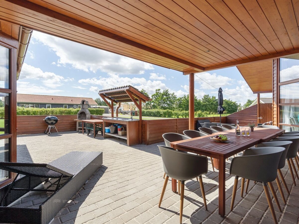 A spacious terrace is shown, featuring a wooden table surrounded by several chairs. A barbecue area is visible, along with a shaded seating area. Natural light floods the space, highlighting the attractive outdoor setting.