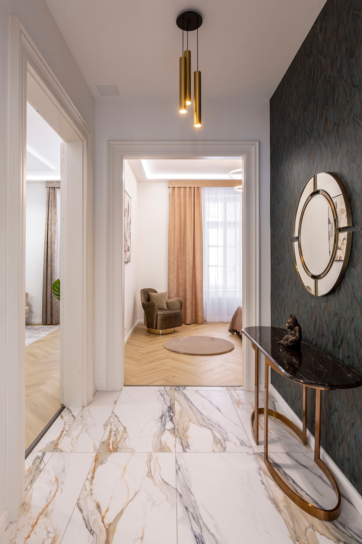 A hallway is showcased, featuring a stylish console table with a decorative statue. Elegant light fixtures hang from the ceiling, illuminating the space. Soft, neutral-toned curtains frame the windows, while a patterned wall adds a touch of sophistication to the environment.