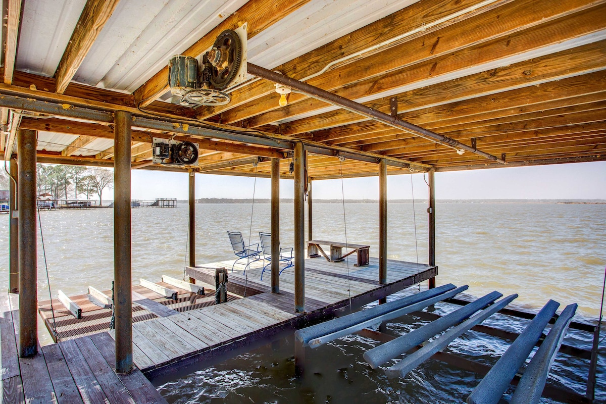 A private dock extends over Cedar Creek Lake, supported by wooden beams. Two chairs are positioned at one end, providing a serene spot for relaxation. Boats are accessible via a set of wooden slats submerged in the water, offering direct lake access.