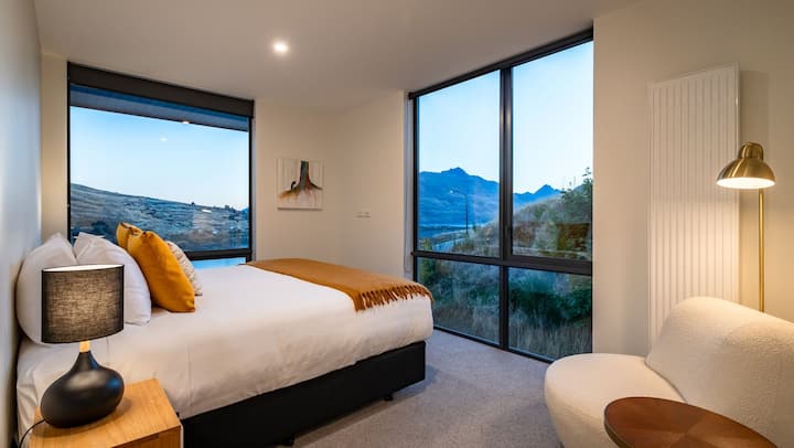 Das Hauptschlafzimmer verfügt über ein luxuriöses Kingsize-Bett, ein eigenes Bad mit einer ebenerdigen Dusche und einen geräumigen Kleiderschrank mit atemberaubendem Blick auf den See und die Berge.