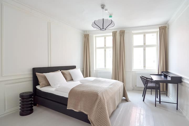 Dve svetlé a pohodlné spálne majú elegantné biele steny, biele podlahy, vysoké stropy, vysoké stropy a krásne béžové záclony, ktoré vytvárajú útulnú a príjemnú atmosféru.