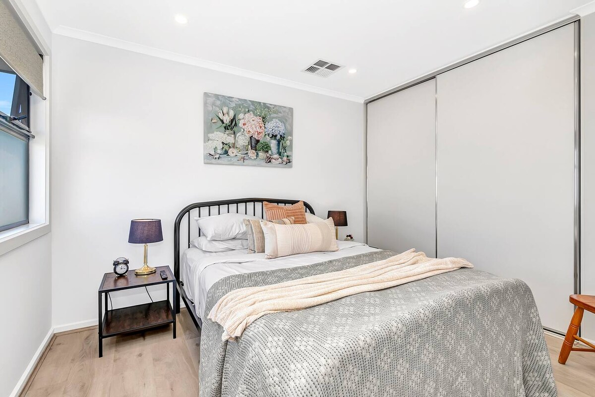 La habitación principal cuenta con una cama tamaño queen con mesas auxiliares y lámparas, así como batas empotradas y un televisor montado en la pared. 