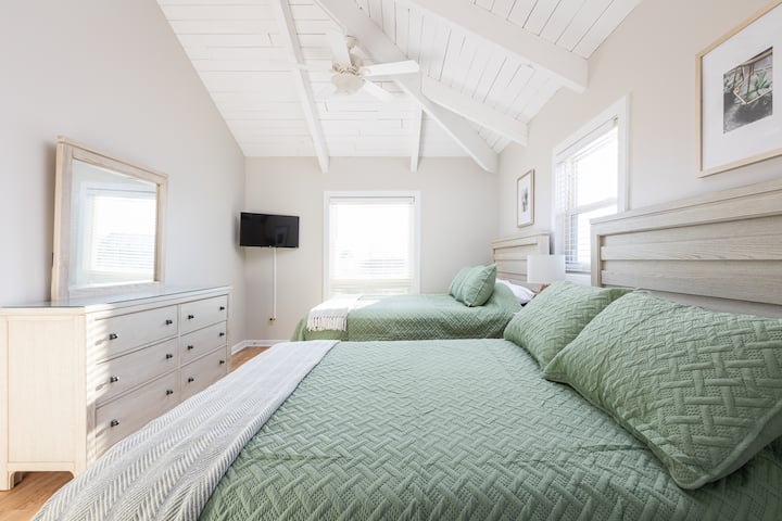 Soveværelse med queensize-dobbelt- og enkeltseng, tv, loftventilator, kommode og spejl