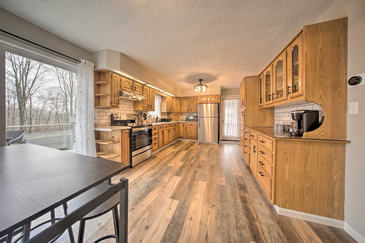 A spacious kitchen features wooden cabinetry and a combination of countertop and built-in appliances. Natural light filters in through a large window, illuminating the tiled backsplash. An adjacent dining area is visible, enhancing the overall functionality of this inviting space.