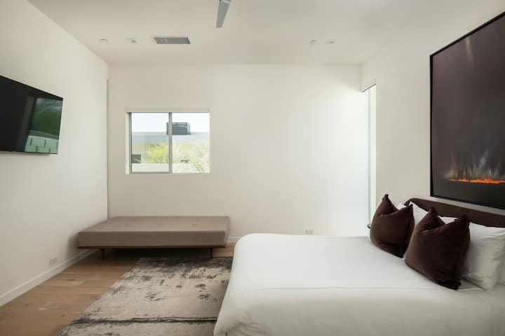 Još jedna mirna spavaća soba sa bračnim krevetom, udobnim dnevnim krevetom, modernom umjetnošću i mekim osvjetljenjem.