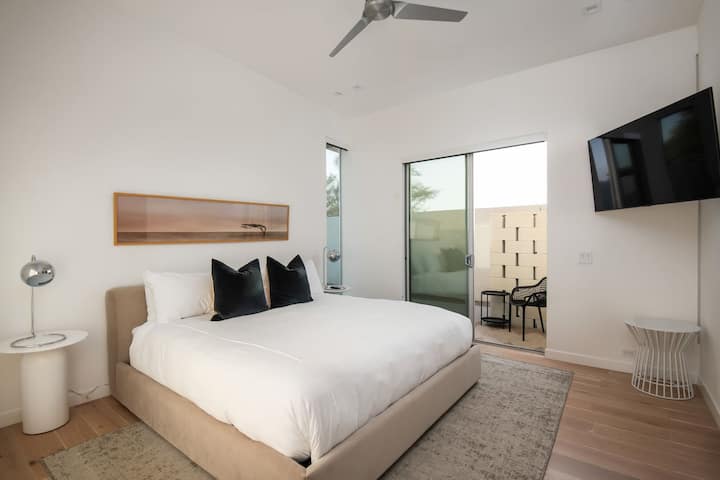 एक आरामदायक बेड, स्मार्ट टीवी और आउटडोर पैटियो तक निजी स्लाइडिंग डोर ऐक्सेस के साथ एक उज्ज्वल और शांत क्वीन बेडरूम।