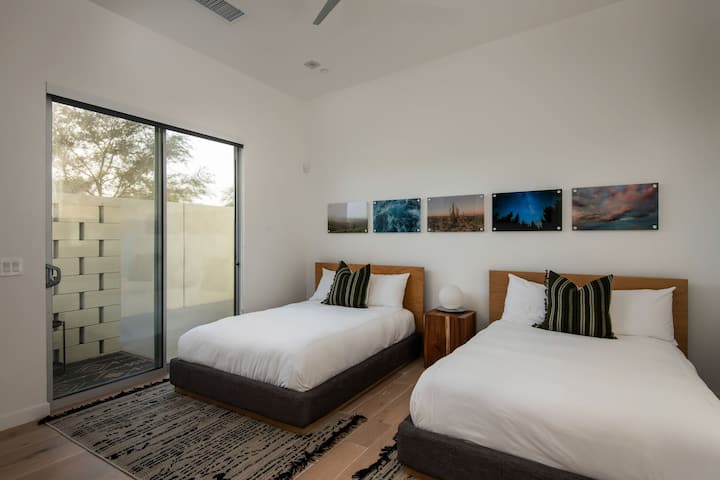 फ़्लेक्सिबल ट्विन बेडरूम, जिसमें जीवंत कलाकृति, दो आरामदायक बिस्तर और शांत रेगिस्तानी अहाते के लिए एक निजी निकास है।