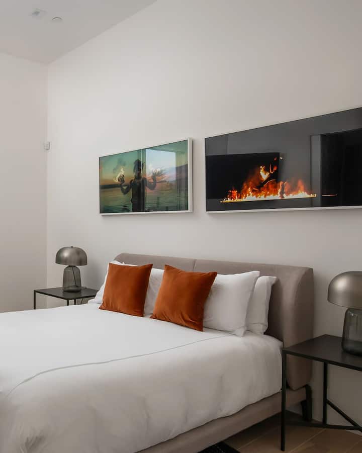 Una cómoda suite con cama tamaño queen con arte contemporáneo e iluminación junto a la cama para un retiro nocturno tranquilo.