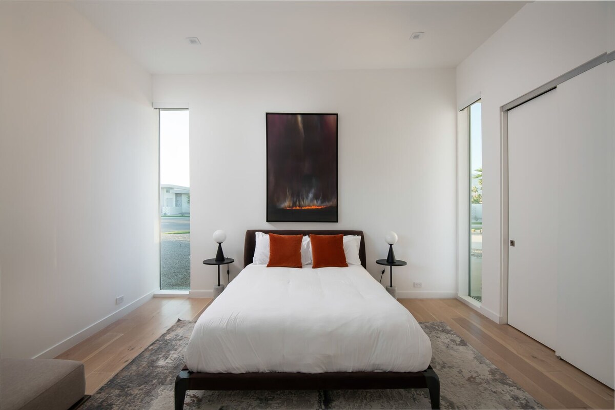 Un dormitorio queen luminoso y artístico con grandes ventanales, obras de arte llamativas y un armario profundo.