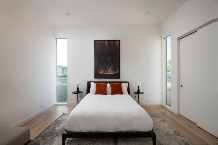 Un dormitorio tamaño queen luminoso y artístico con grandes ventanales, obras de arte llamativas y un armario profundo.