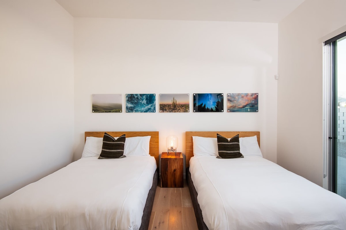 Una vista en primer plano de las cómodas camas de la habitación doble, la iluminación individual y la vibrante pared de la galería.