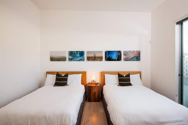 Una vista de cerca de las cómodas camas del dormitorio doble, la iluminación individual y la vibrante pared de la galería.