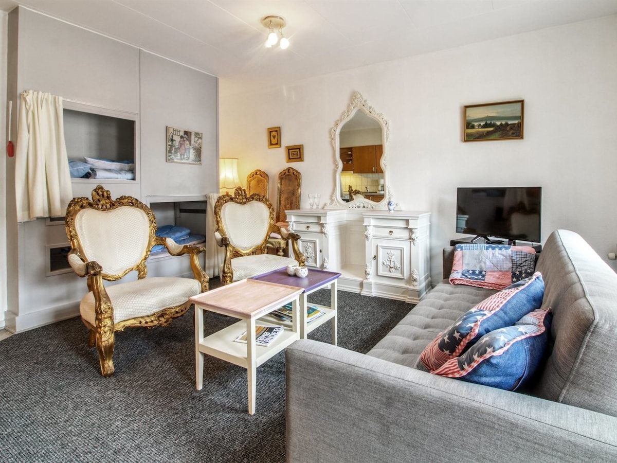 The living room features two ornate armchairs and a modern sofa, offering a mix of classic and contemporary styles. A small coffee table sits at the center, surrounded by an inviting atmosphere. A television is positioned for viewing, and a decorative mirror adds depth to the space.