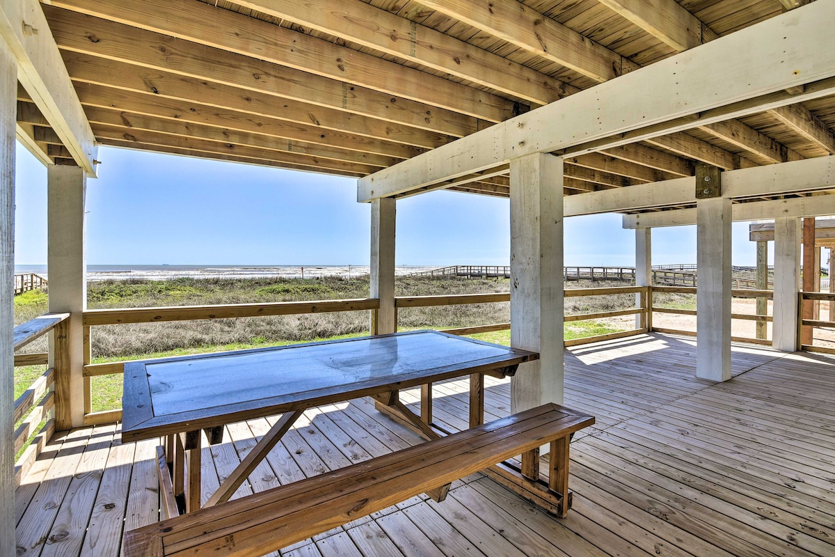 A spacious outdoor deck area features a large picnic-style table with attached seating, surrounded by wooden posts. The calming view of the beach and ocean can be seen through the open design, allowing natural light to flood the space.