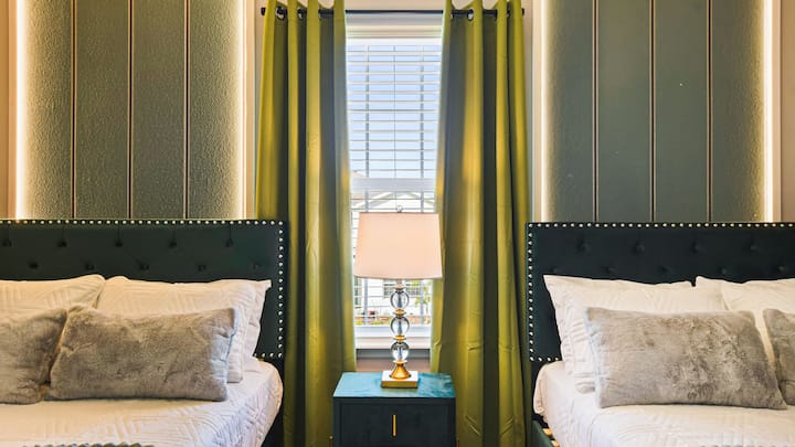 Მყუდრო საძინებელი ორადგილიანი საწოლებით, რბილი განათებითა და ელეგანტური მწვანე აქცენტებით.