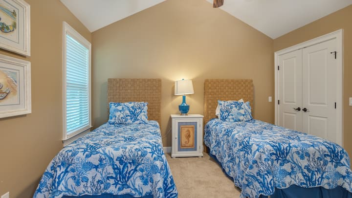 Оваа светла спална соба за гости има засводени тавани и два одделни кревета со постелнина инспирирана од крајбрежјето.