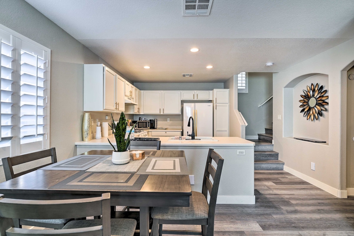 A well-lit kitchen and dining area are present, featuring white cabinetry and modern appliances. A dining table with four chairs is set nearby. The space is designed with neutral tones and wood-like flooring, adding to the inviting atmosphere. Stairs are visible leading to the upper level.
