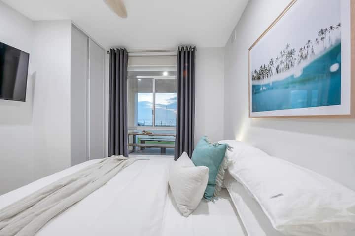 غرفة النوم 1 مع إطلالة جميلة على الشاطئ، وتشمل مروحة سقف وتلفزيون وخزانة ملابس.