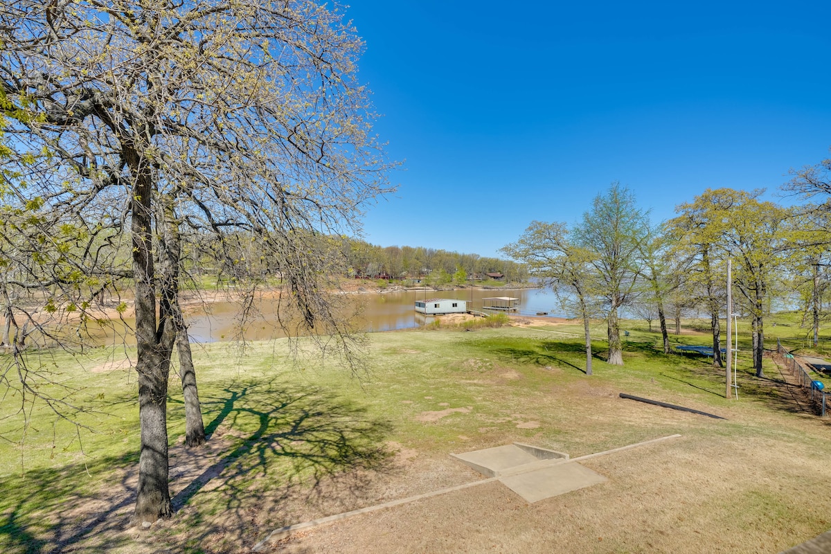 A spacious outdoor area features a well-maintained grassy lawn bordered by trees, with a view of Eufaula Lake in the distance. The calm water reflects the clear blue sky, creating a peaceful setting for outdoor activities.