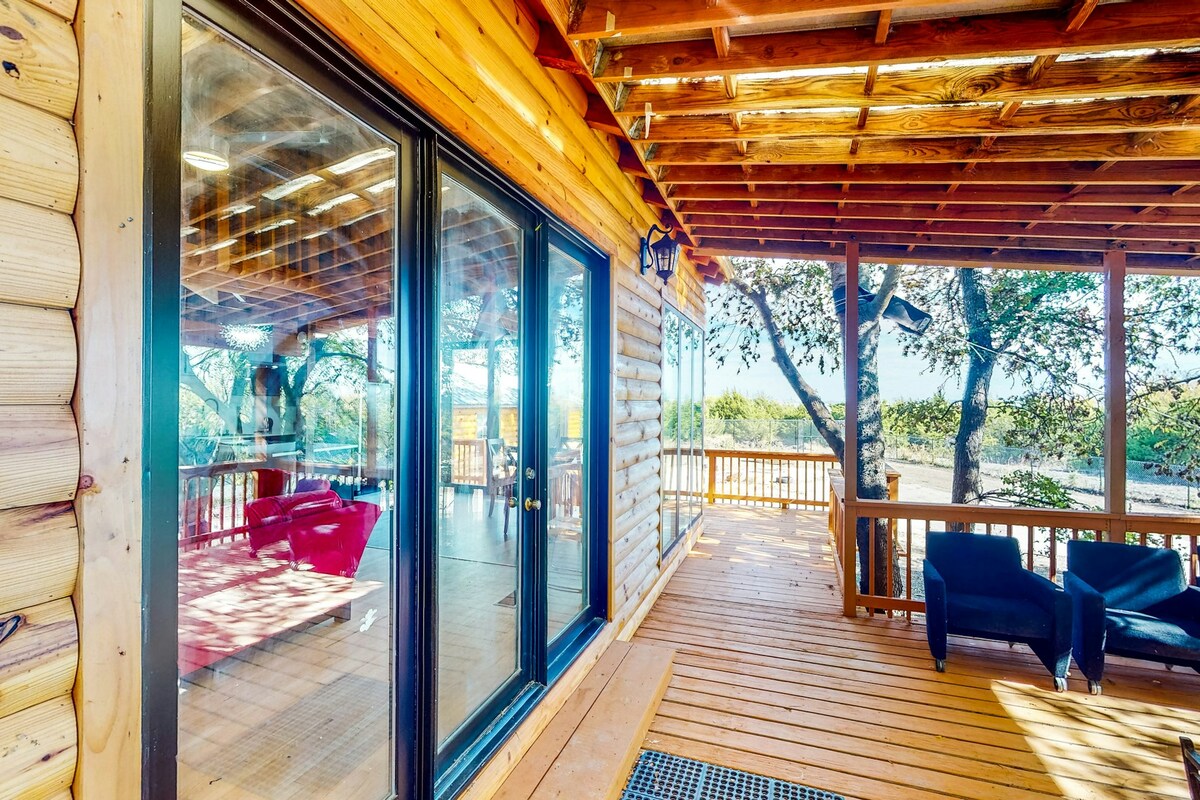 A spacious outdoor deck is lined with wood flooring and features multiple seating areas. Large glass doors provide a view of the interior, while trees surround the area, creating a natural setting. The space is ideal for relaxation and entertainment.