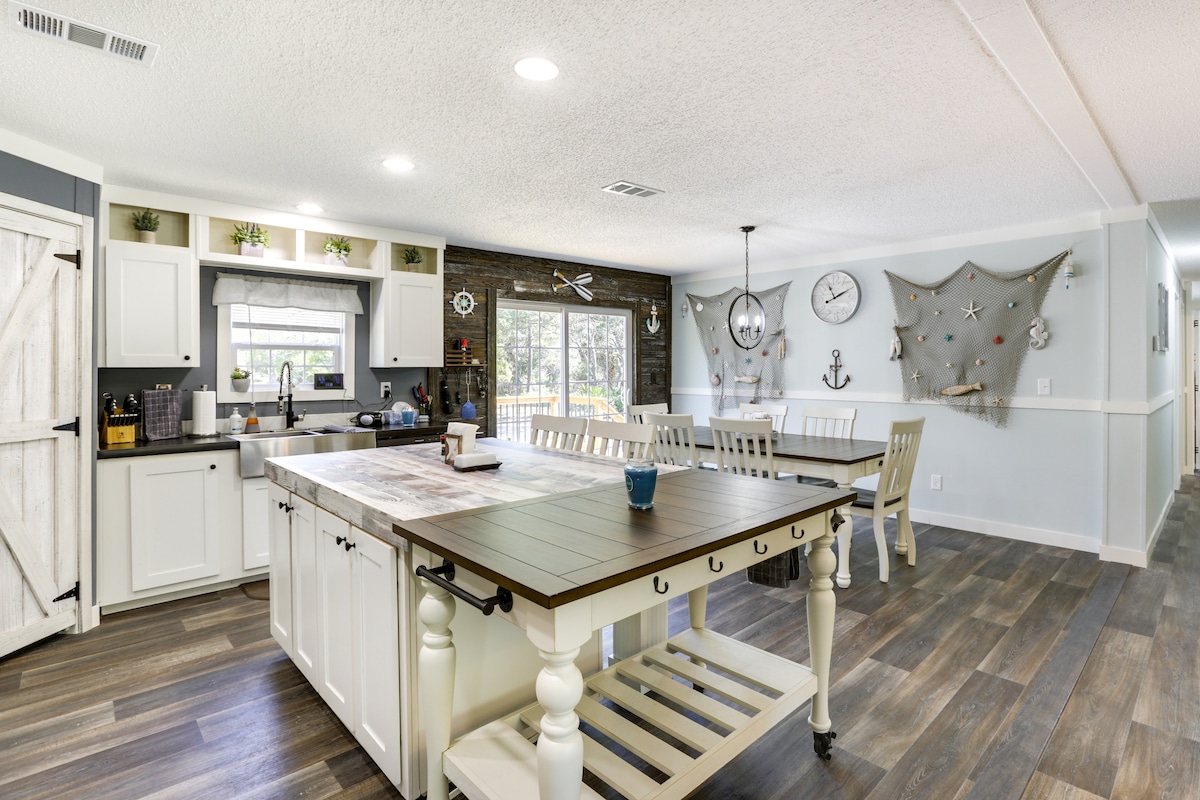 An open-concept kitchen and dining area is presented, featuring a spacious island with a wooden top. A dining table with several chairs is positioned nearby, adorned with nautical decor and large windows that bring in natural light.