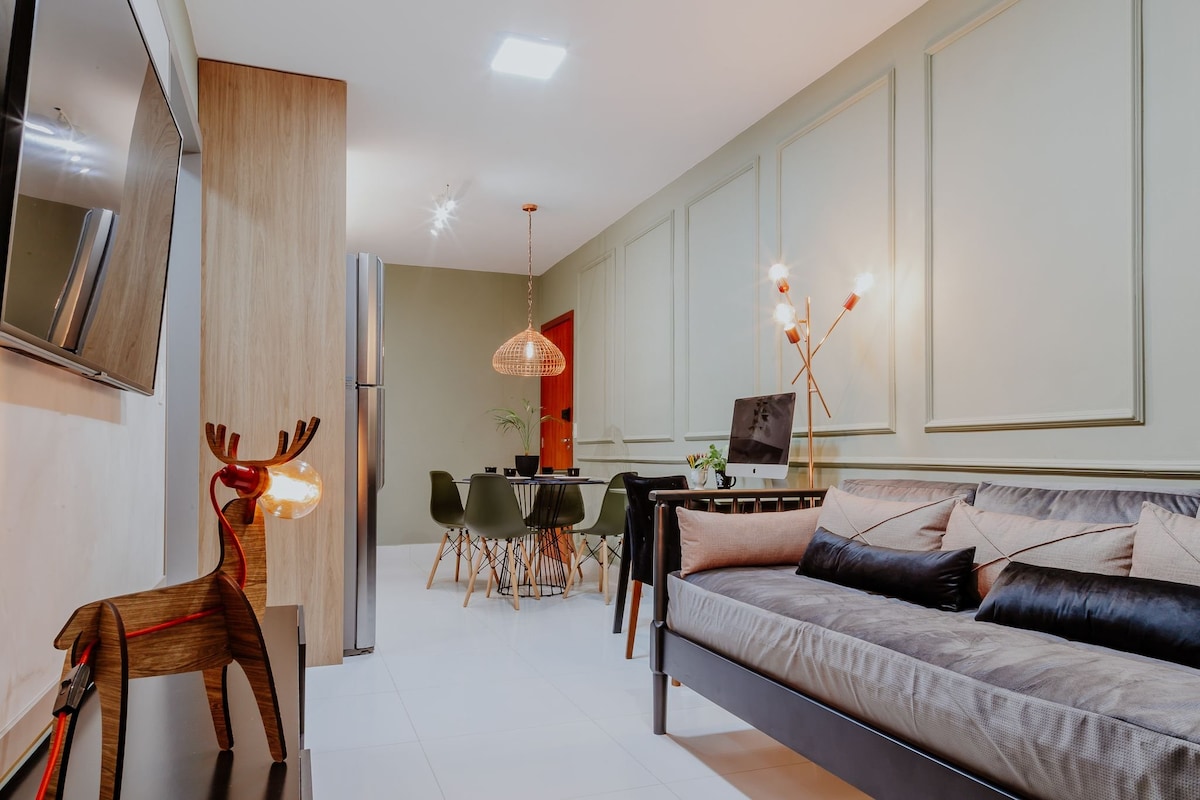 A stylish living area features a sleek sofa with decorative cushions, complemented by a wooden accent piece shaped like a deer. A modern dining table is visible in the background, surrounded by elegant chairs, with a warm glow from the decorative lighting.