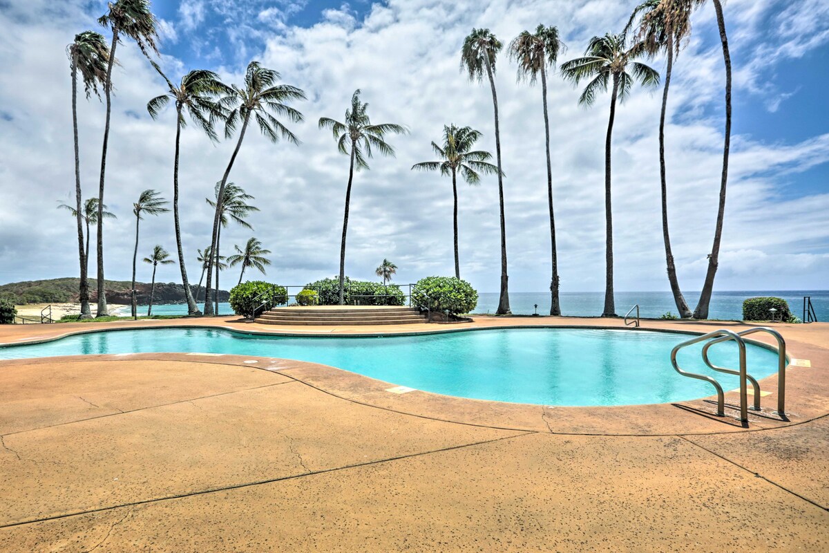 An outdoor community pool is displayed, surrounded by palm trees swaying gently. The clear blue water reflects the sky, while lounge areas are available nearby. Steps lead into the pool, providing easy access for relaxation and enjoyment of the scenic coastal view.