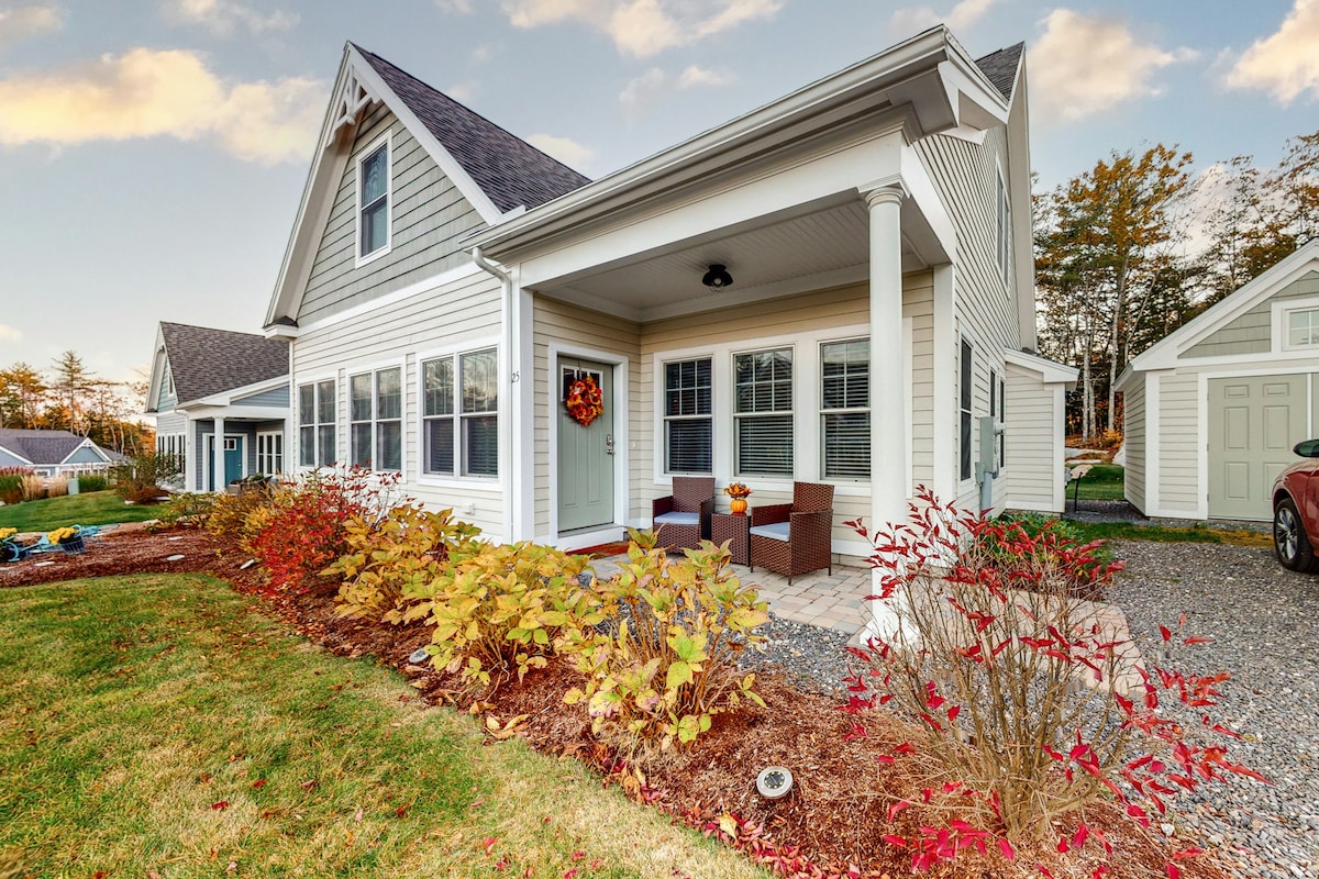 The exterior of the home features a charming front porch with two cushioned armchairs. Colorful foliage and landscaping surround the entryway, complemented by bright decorative accents. Large windows allow natural light to fill the interior, enhancing the inviting appeal of this cottage-style residence.