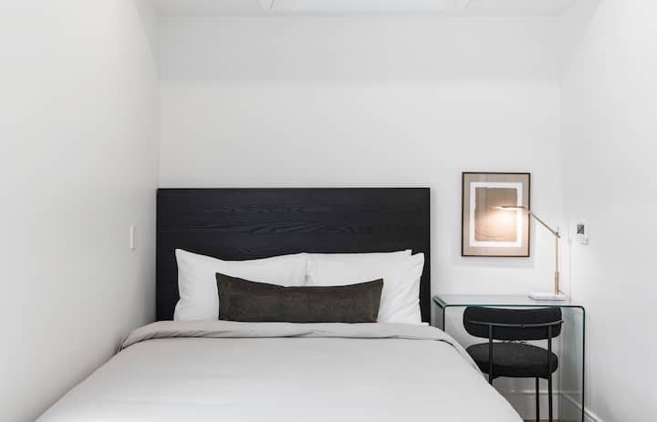 Queen ‑ ის ზომის საწოლი, რომელიც გამოწყობილია კალიფორნიის დენის დიზაინის თეთრეულით. Სამუშაო სივრცე სამუშაო მაგიდით 