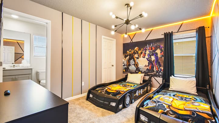 Transformatorių tematikos dvivietis kambarys su automobilinėmis lovomis ir drąsiu apšvietimu jauniems didvyriams.