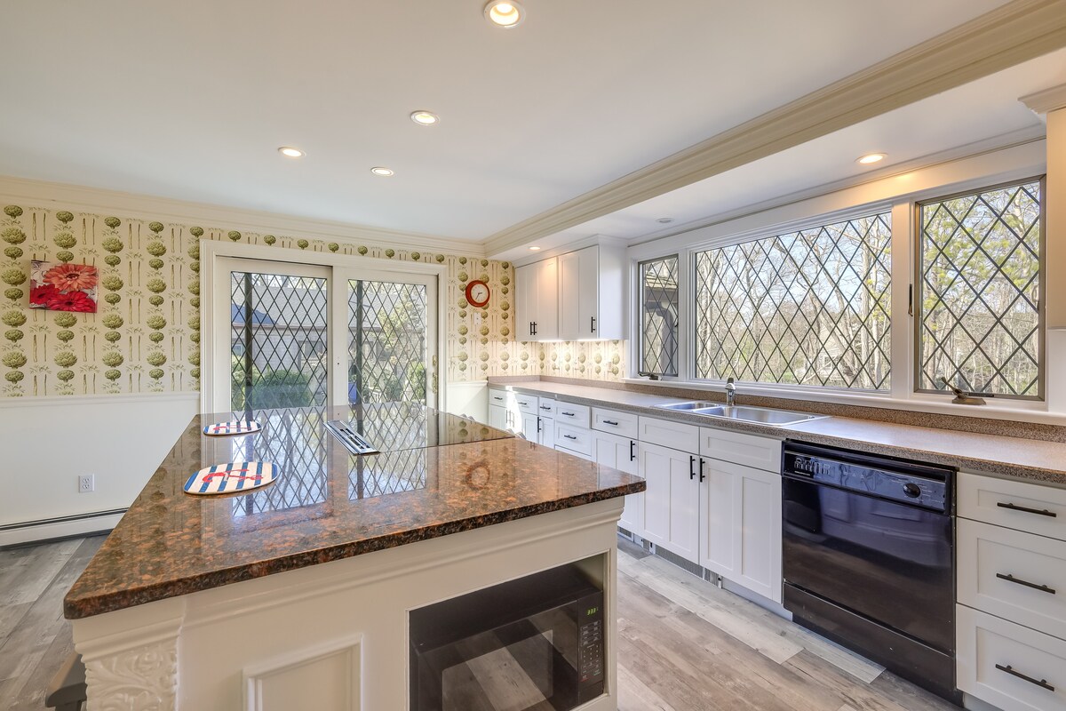 The kitchen features a polished granite countertop with a breakfast bar, complemented by bright white cabinetry. Ample natural light enters through diamond-patterned windows, illuminating the space. A black dishwasher is positioned next to the sink, contributing to the functional layout.